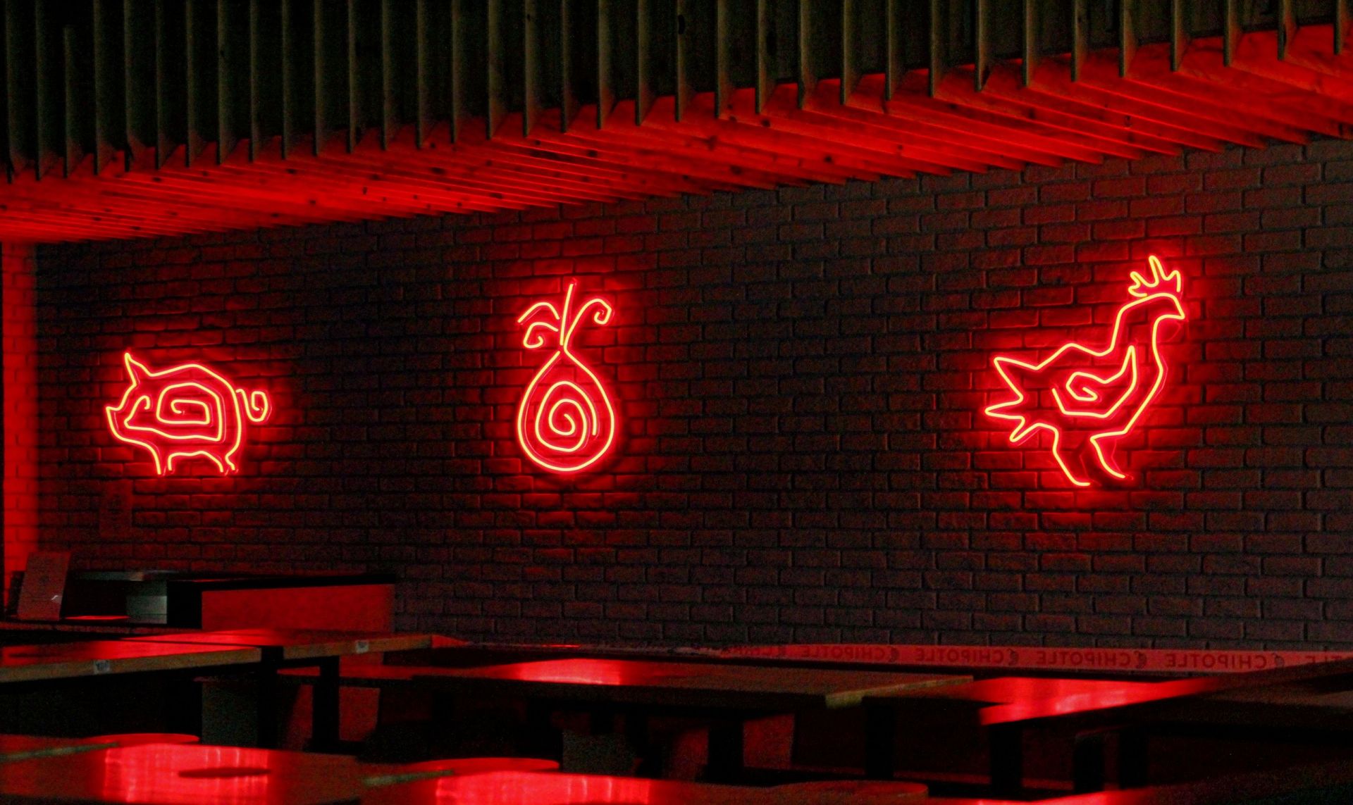 Red neon pig, onion, and rooster signs glowing on a brick restaurant wall